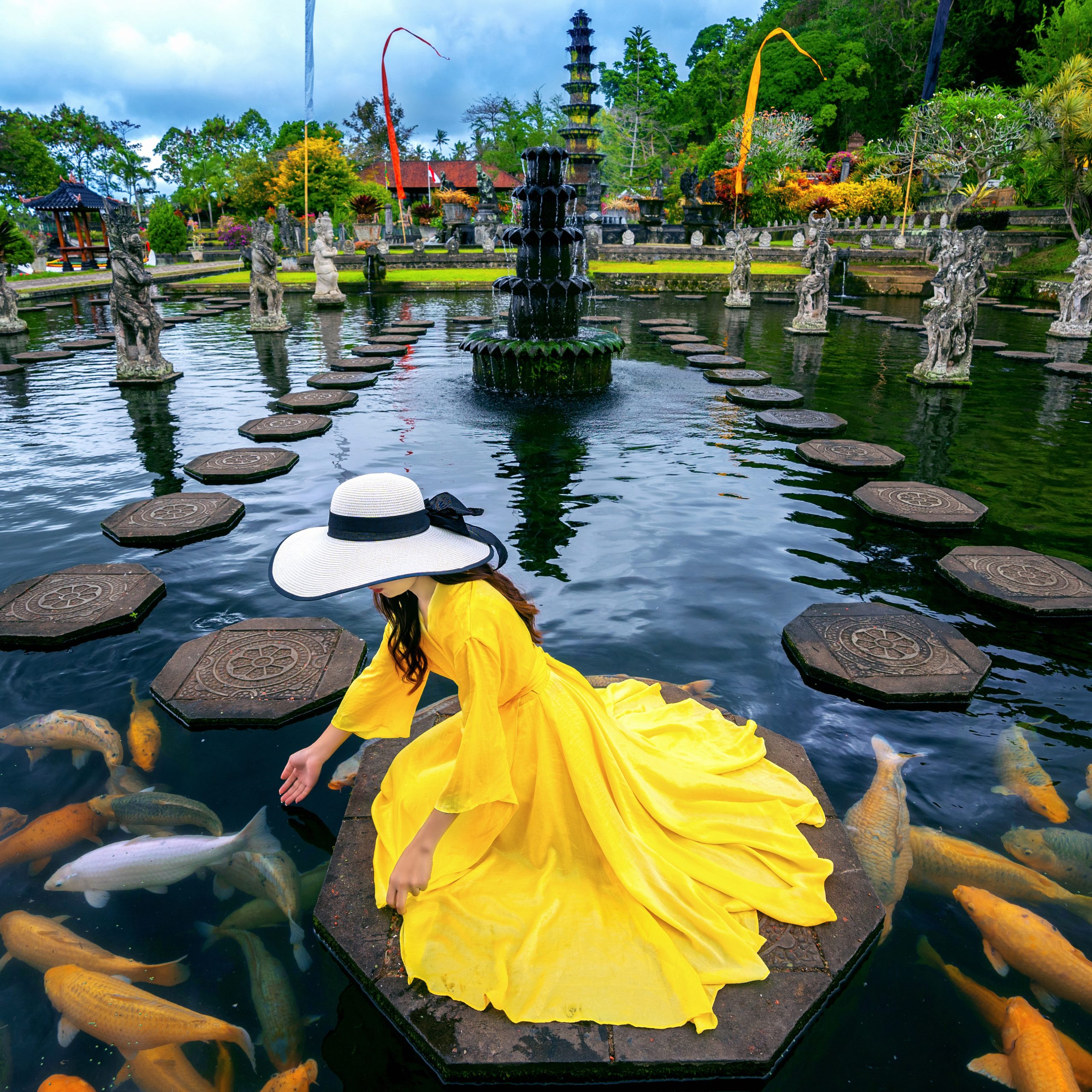 Woman feeding colorful fish in pond at Tirta Gangga Water Palace in Bali, Indonesia.