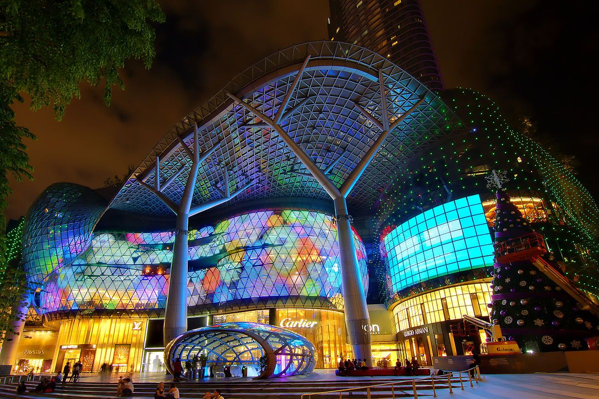 A beautifully lit building stands against the night sky, surrounded by illuminated trees and a festive Christmas tree, creating a vibrant outdoor landscape in the city.