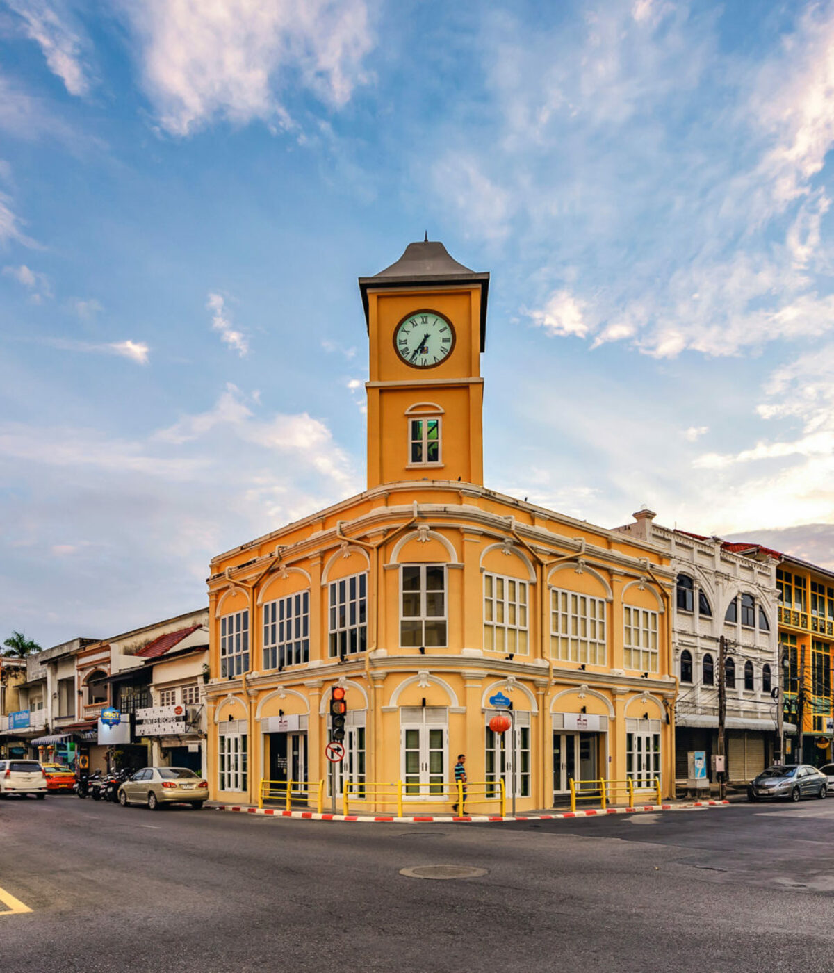 Historic yellow building with a clock tower on a street corner under a cloudy sky.