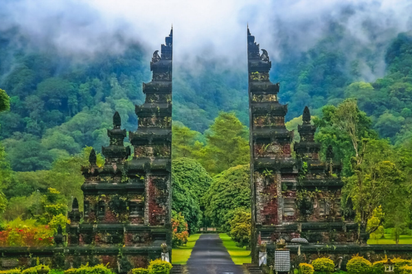 The entrance to a temple in Ubud, Bali, featuring intricate carvings and lush greenery surrounding the pathway.