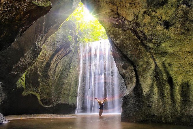 A person stands before a majestic waterfall, surrounded by lush greenery and mist rising from the cascading water.