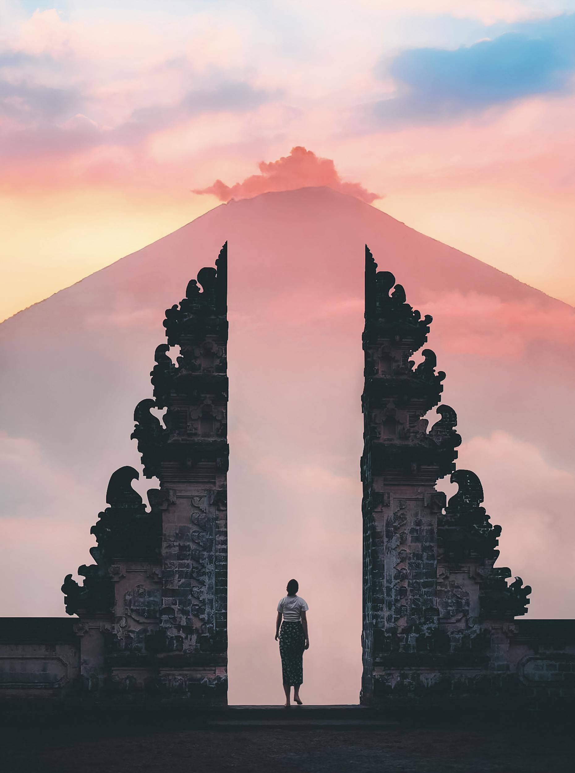 A person stands before an archway, framed by a majestic mountain in the background, showcasing a serene landscape.