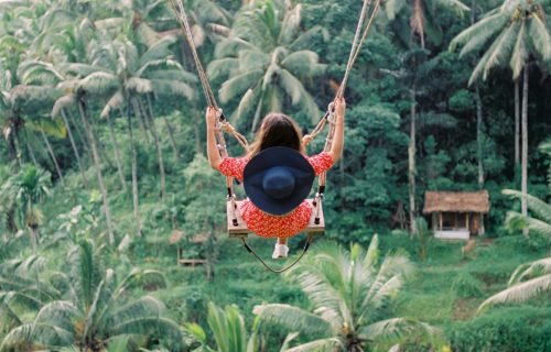 A woman joyfully swings amidst lush greenery in a vibrant jungle setting.
