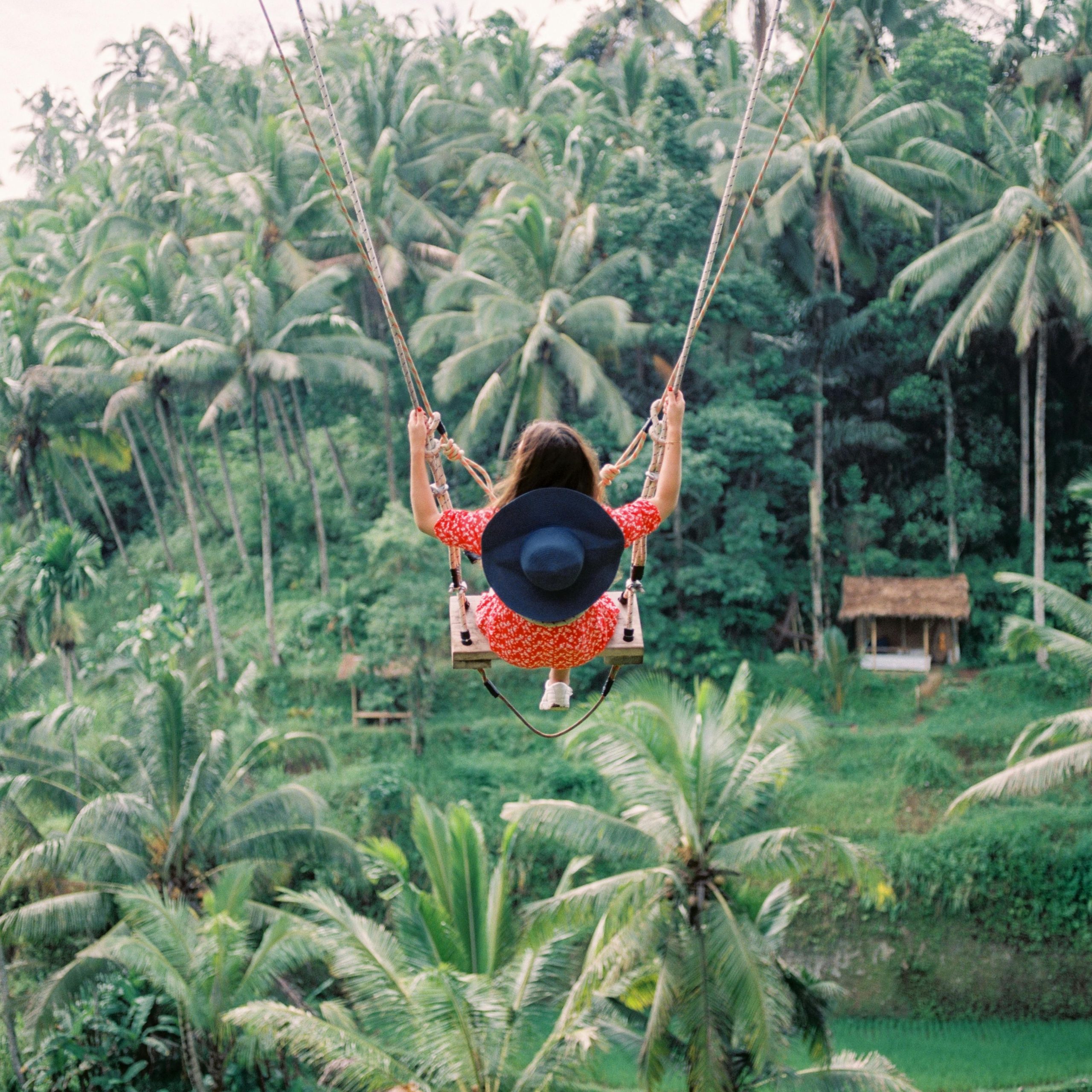 A woman joyfully swings amidst lush greenery in a vibrant jungle setting.