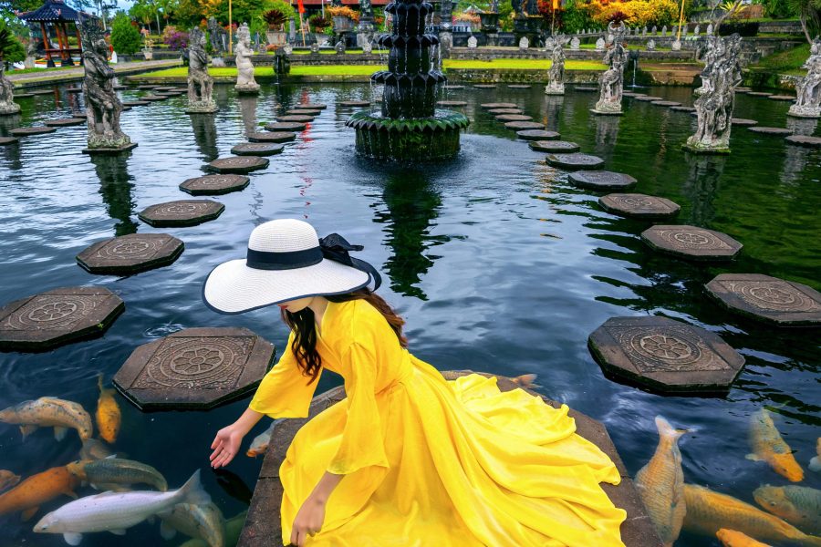 Woman feeding colorful fish in pond at Tirta Gangga Water Palace in Bali, Indonesia.