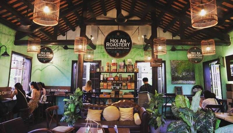 Interior of Hoi An Roastery with customers, rustic decor, and wooden ceiling.