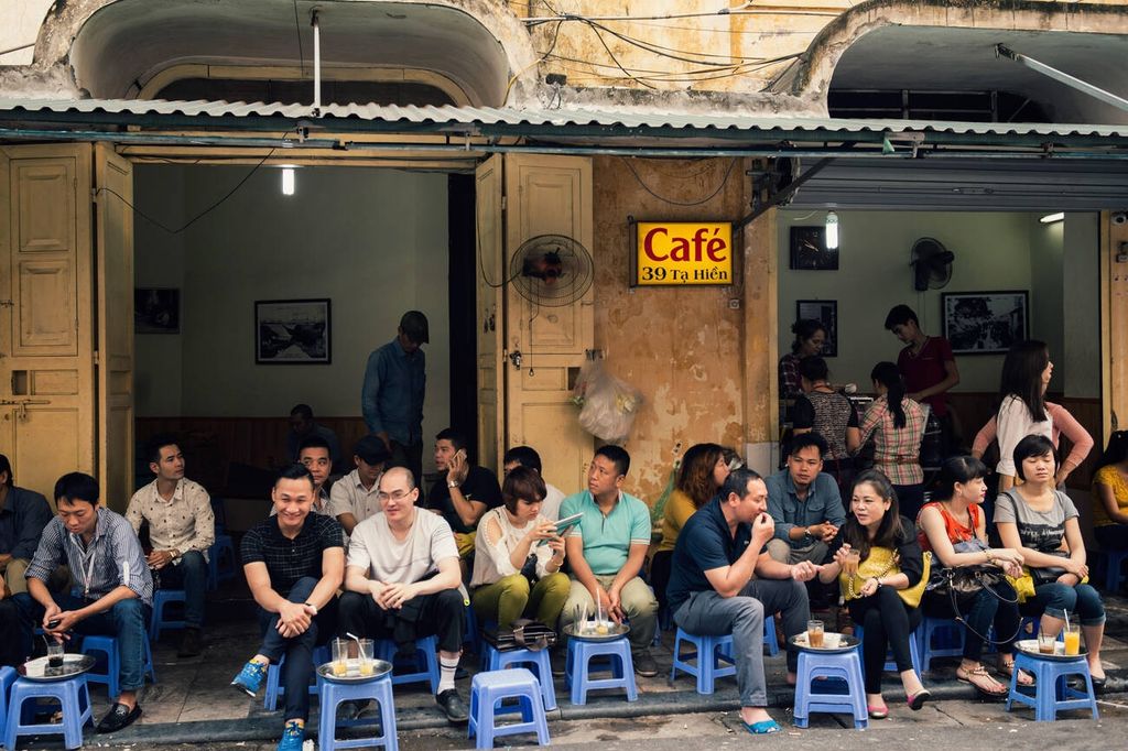 People sitting on small stools at a busy street café.