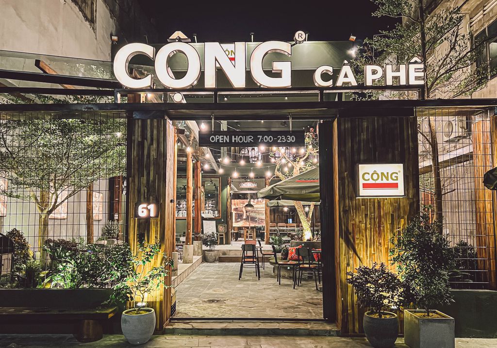 Entrance of 'CỘNG CÀ PHÊ' coffee shop at night, with lit-up sign and open door.