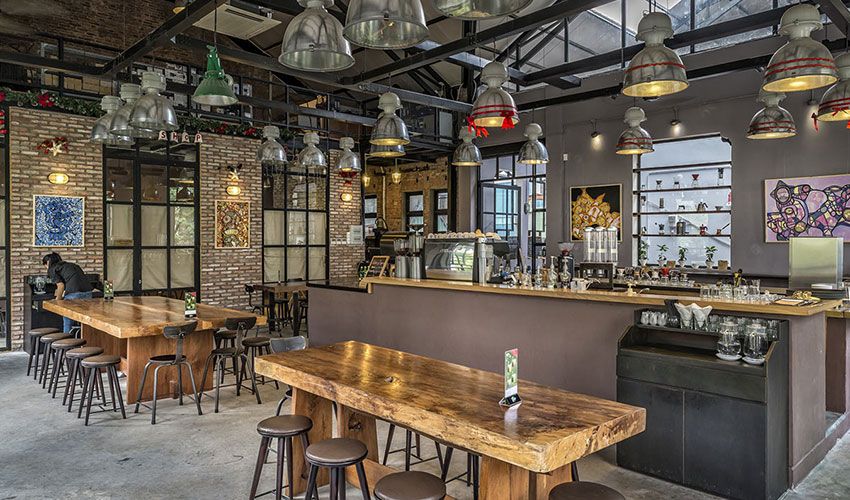 Interior of an industrial-themed cafe with wooden tables, pendant lights, and a person sitting.