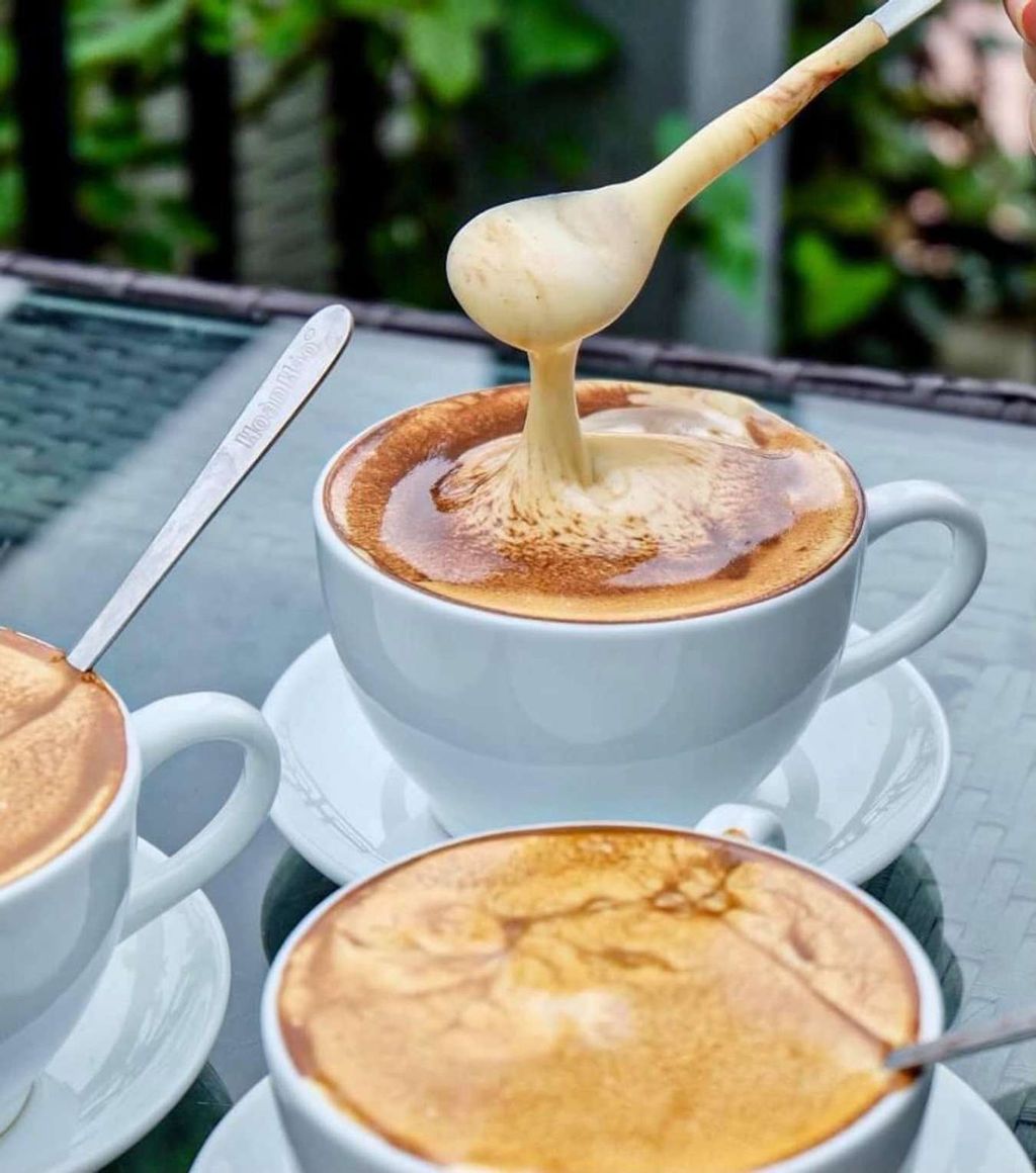 Three cups of cappuccino with froth being lifted by a spoon.