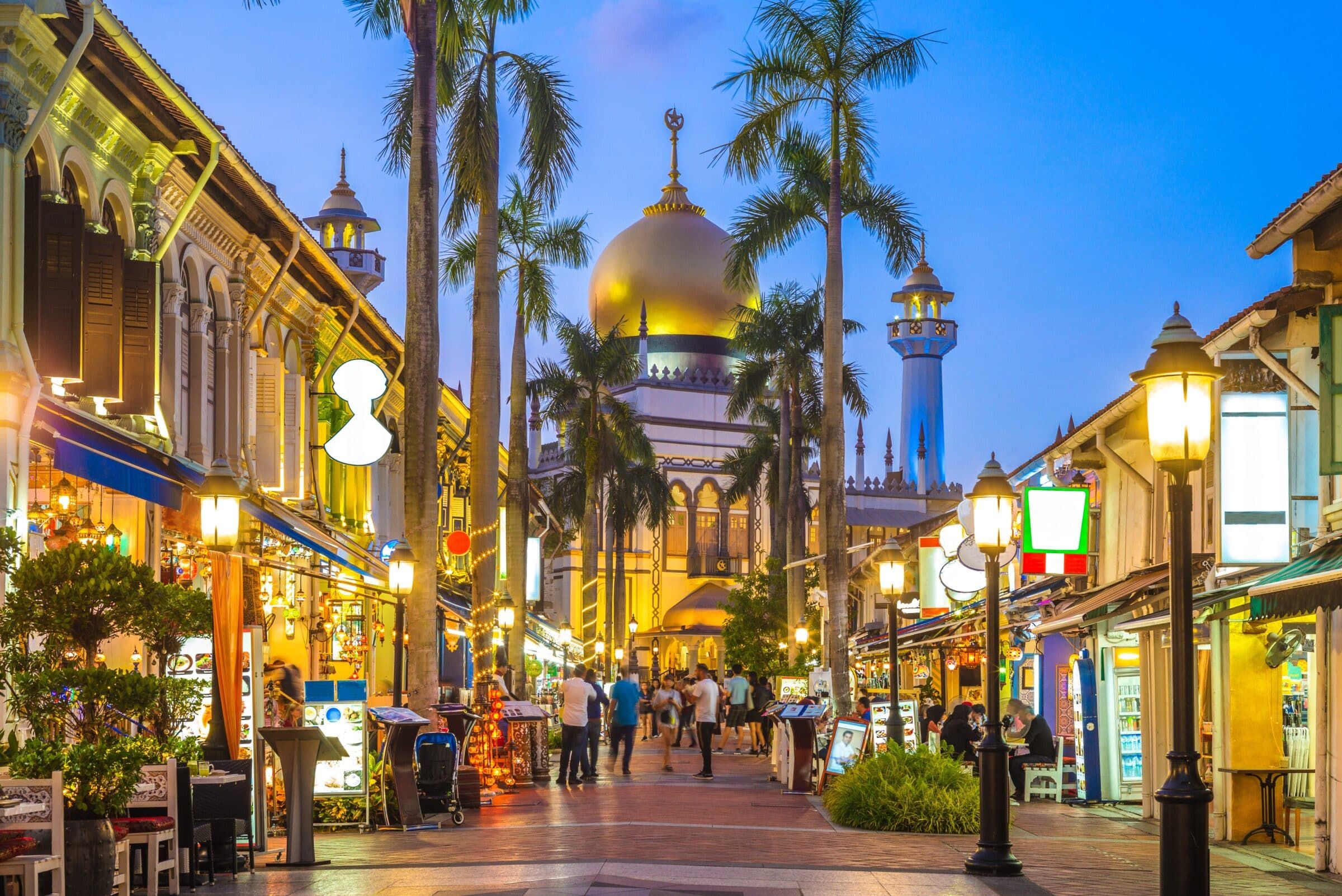 A street lined with palm trees and buildings, illuminated at night.