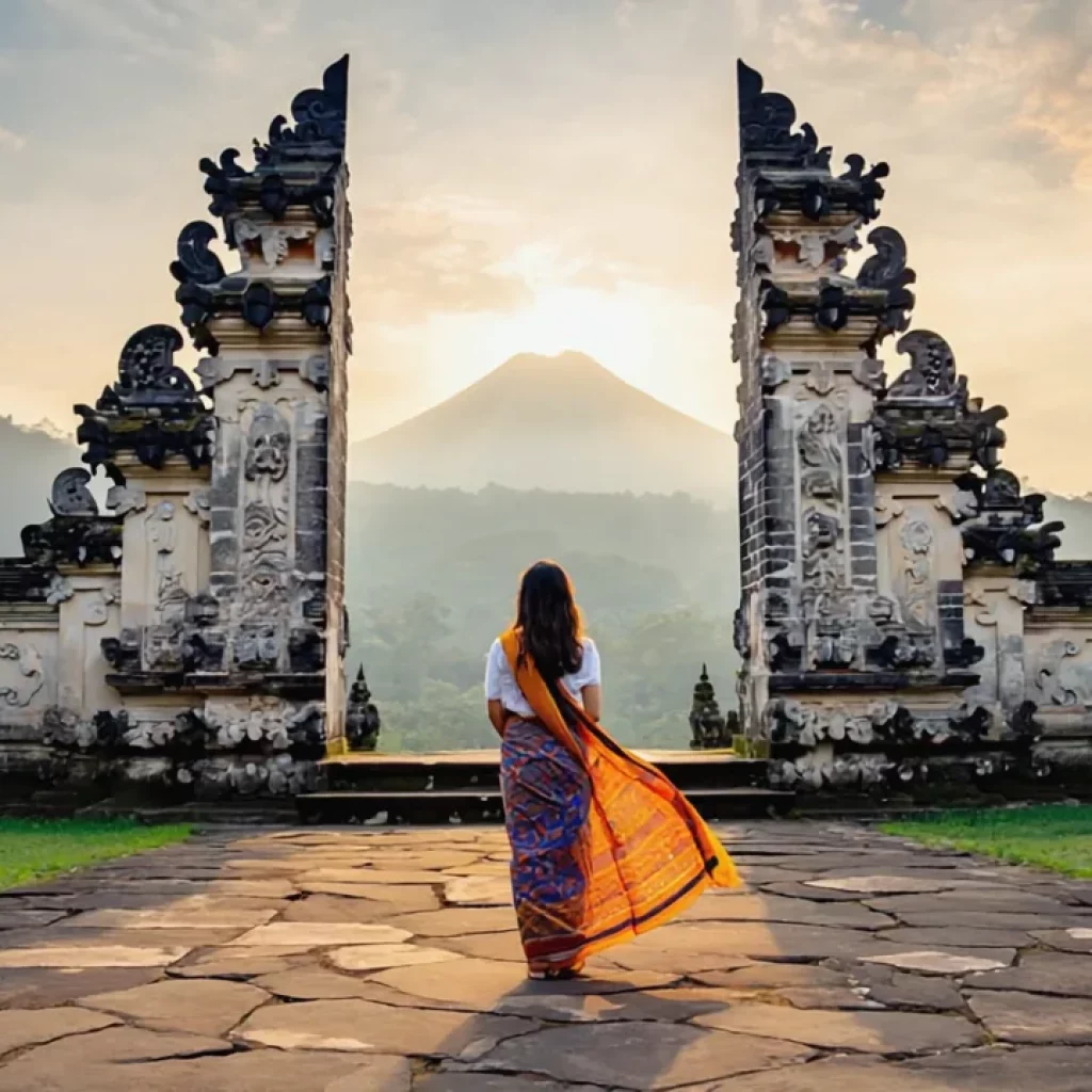 Sunrise view at Lempuyang Temple, Bali, dramatic Mount Agung in background, morning mist curling around stone gates, woman in colorful sarong posing peacefully, realistic photography, vibrant colors, soft golden light, high detail